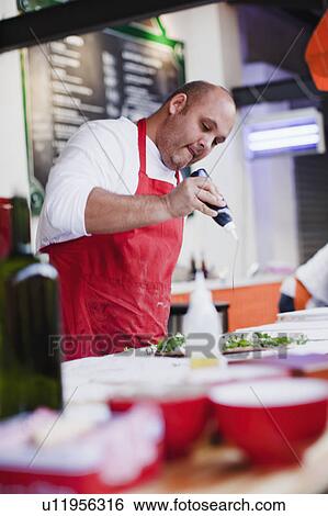 Stock Photograph - Chef drizzling oil over pizza in kitchen. Fotosearch
