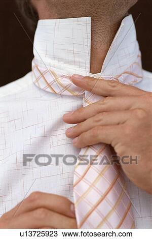 Stock Image - Close up of businessman adjusting tie. Fotosearch