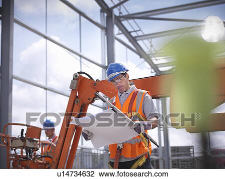 Stock Image - Construction worker reading blueprints. Fotosearch