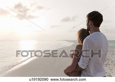 Stock Image - Couple admiring horizon at beach. Fotosearch