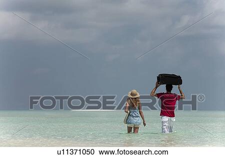 Couple carrying luggage into sea View Large Photo Image Stock Image - Couple carrying luggage into sea. Fotosearch