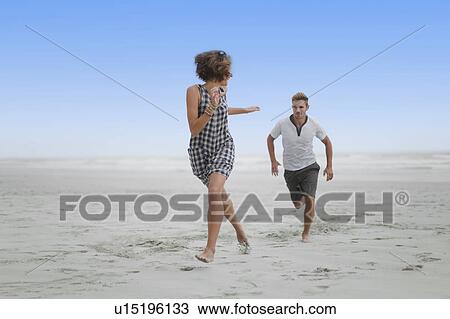Stock Image - Couple chasing each other on beach. Fotosearch