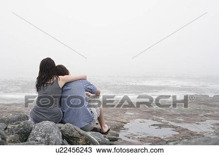 Stock Image - Couple hugging on rocky beach. Fotosearch