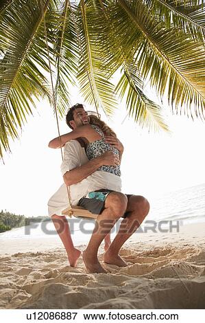 Stock Photo - Couple hugging on swing at beach. Fotosearch