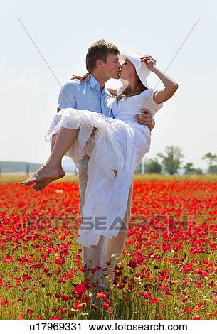Stock Image - Couple kissing in field of poppies. Fotosearch