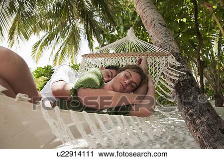 Stock Image - Couple laying in hammock on beach. Fotosearch