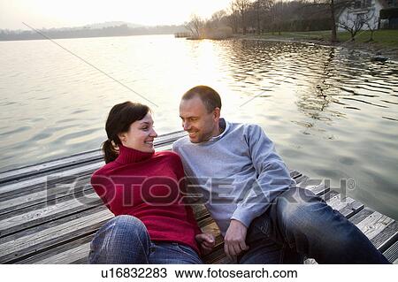 Stock Image - Couple laying on jetty over lake. Fotosearch