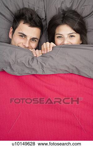 Couple peering out from under blanket View Large Photo Image Stock Photo - Couple peering out from under blanket. Fotosearch