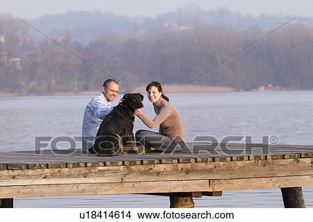 Couple petting dog on jetty over lake View Large Photo Image Picture - Couple petting dog on jetty over lake. Fotosearch