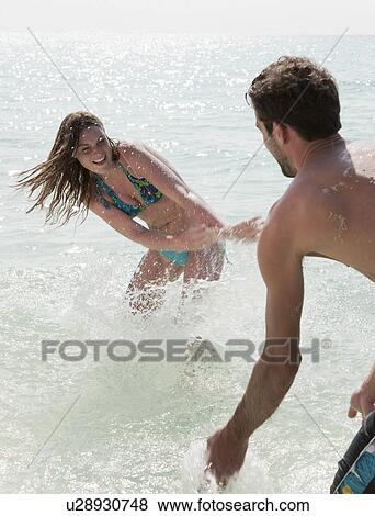Couple playing in water on beach View Large Photo Image Stock Photo - Couple playing in water on beach. Fotosearch