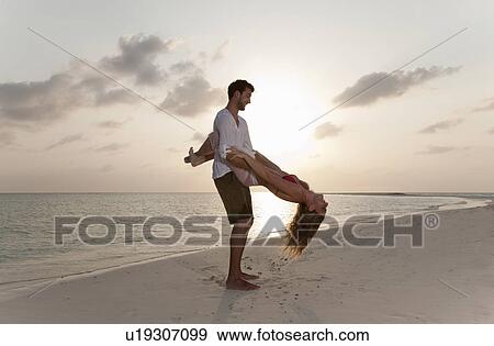 Stock Photo - Couple playing on beach at sunset. Fotosearch