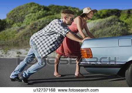 Stock Photo - Couple pushing broken down car. Fotosearch