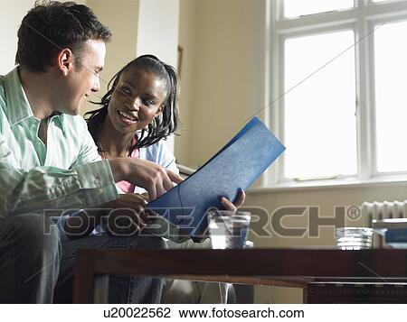 Stock Image - Couple reading folder in living room. Fotosearch