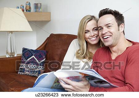 Stock Image - Couple reading magazine together on sofa. Fotosearch