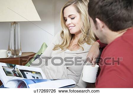 Couple reading magazine together on sofa View Large Photo Image Stock Photograph - Couple reading magazine together on sofa. Fotosearch