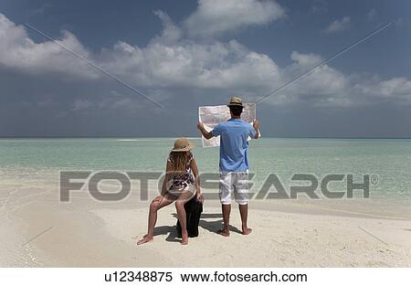 Stock Photography - Couple reading map on tropical beach. Fotosearch
