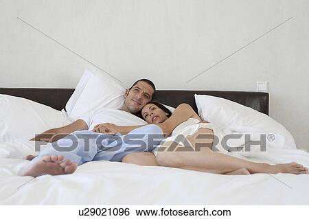 Couple relaxing in bed together View Large Photo Image Stock Photograph - Couple relaxing in bed together. Fotosearch