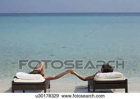 Stock Photo - Couple relaxing on daybeds at beach. Fotosearch