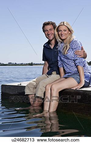 Stock Image - Couple relaxing together on dock. Fotosearch