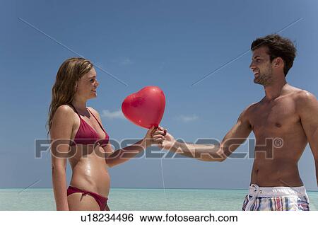 Couple sharing red balloon on beach View Large Photo Image Stock Photograph - Couple sharing red balloon on beach. Fotosearch