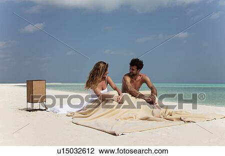 Stock Image - Couple sitting in bed on beach. Fotosearch