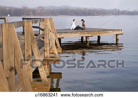 Stock Image - Couple talking on jetty overlooking lake. Fotosearch