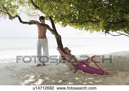 Stock Image - Couple talking under tree on beach. Fotosearch