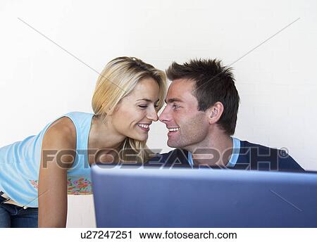 Stock Image - Couple touching noses at laptop. Fotosearch