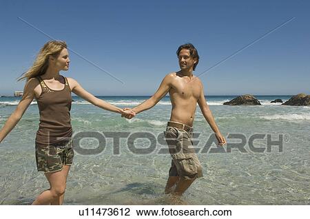 Stock Image - Couple walking hand-in-hand on beach. Fotosearch
