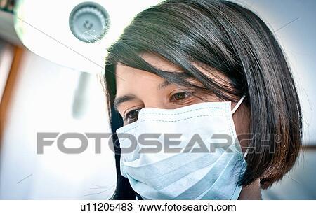 Stock Image - Dentist in face mask working in office. Fotosearch