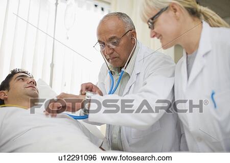 Doctors tending to hospital patient View Large Photo Image Stock Photograph - Doctors tending to hospital patient. Fotosearch