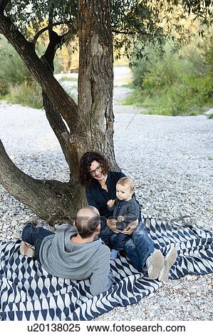 Stock Photography - Family relaxing under tree together. Fotosearch