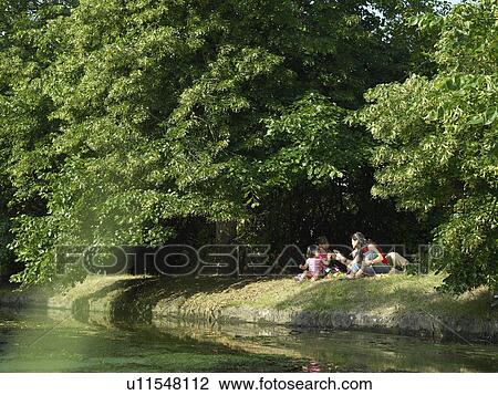 Stock Image - Family sitting on riverbank together. Fotosearch