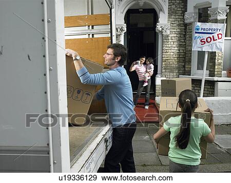 Stock Photo - Family unpacking boxes from moving van. Fotosearch