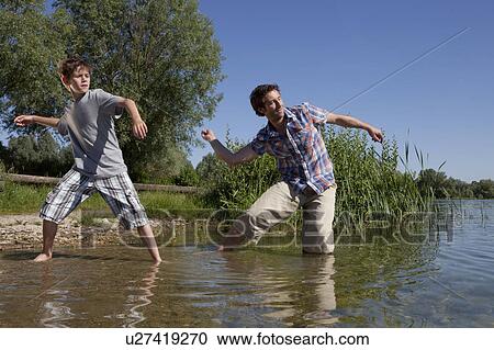 Stock Image - Father and son skipping rocks on lake . Fotosearch