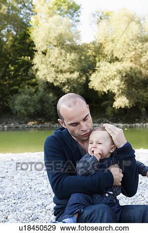 Stock Photo - Father holding crying baby by creek. Fotosearch