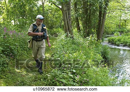 Stock Image - Fisherman walking along river. Fotosearch