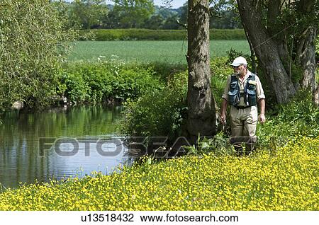 Stock Image - Fisherman walking along river. Fotosearch