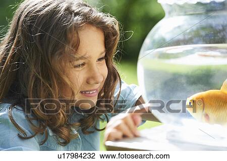 Stock Image - Girl admiring goldfish in bowl. Fotosearch