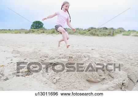 Stock Photograph - Girl destroying sand castle on beach. Fotosearch