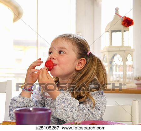 Girl eating a strawberry at table View Large Photo Image Stock Photo - Girl eating a strawberry at table. Fotosearch