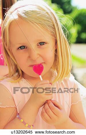 Stock Photography - Girl eating heart-shaped lollipop. Fotosearch