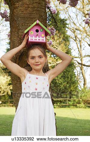 Stock Image - Girl holding birdhouse on her head. Fotosearch
