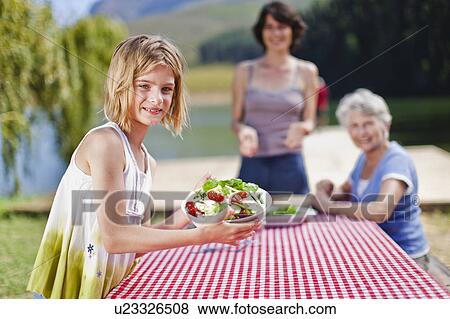 Stock Photo - Girl holding salad at picnic table. Fotosearch