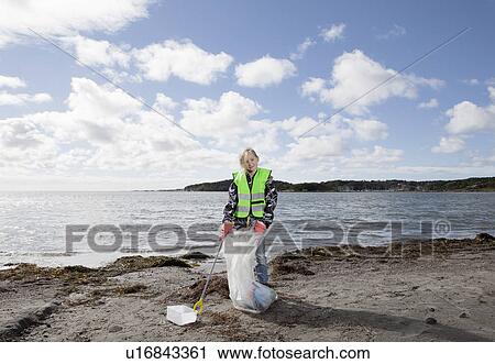 Stock Image - Girl in safety vest cleaning beach. Fotosearch