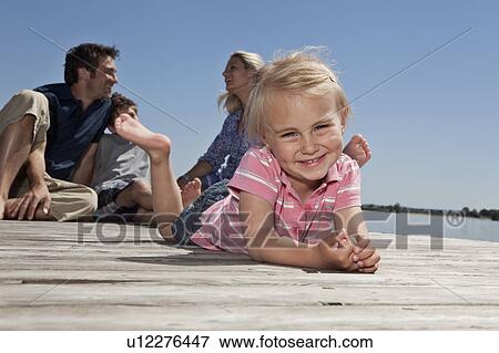 Girl laying on dock with family View Large Photo Image Stock Photo - Girl laying on dock with family. Fotosearch