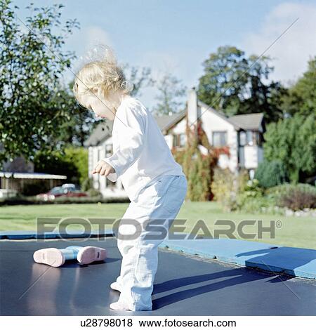 Stock Photo - Girl playing on trampoline in backyard. Fotosearch