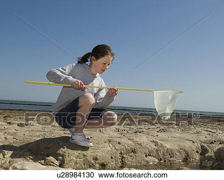 Stock Image - Girl playing with fishing net on beach. Fotosearch