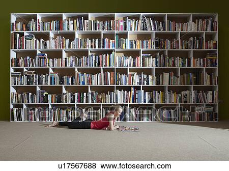 Stock Photo - Girl reading by bookshelves. Fotosearch