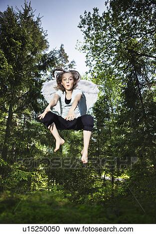 Stock Image - Girl wearing wings and jumping in forest. Fotosearch